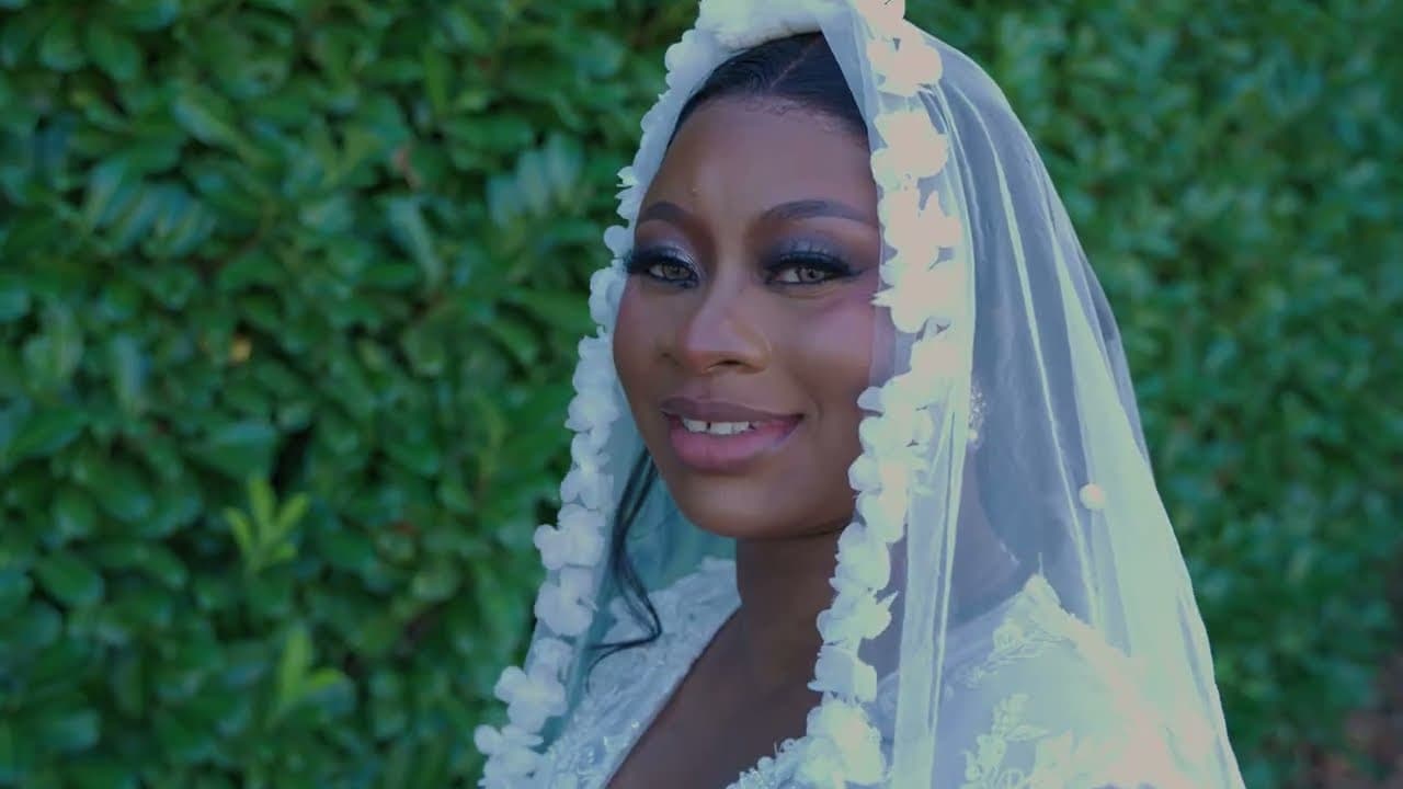 A close portrait of the bride turning to camera, her floral-edged veil framing her face against a dark green hedge.