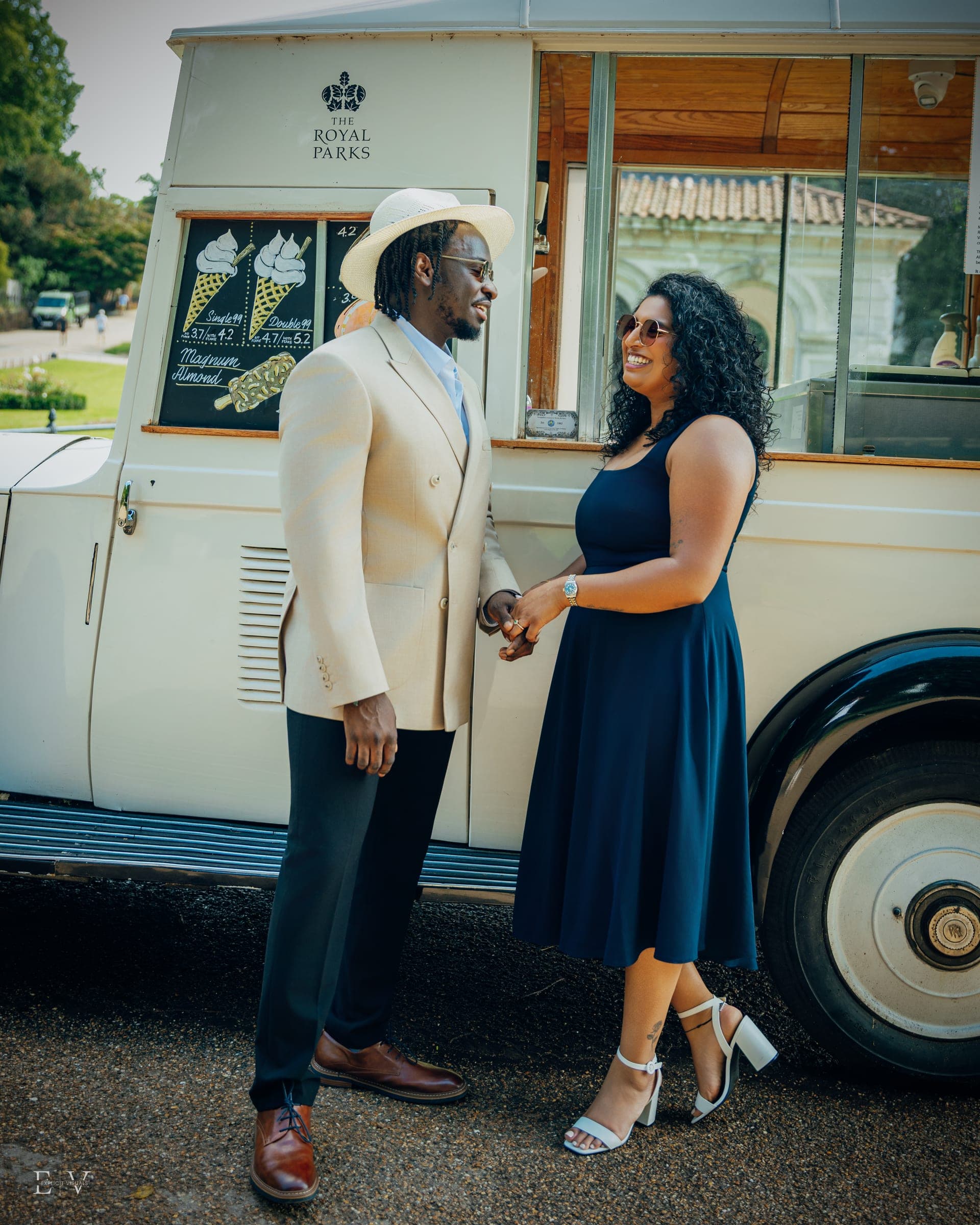 Face to face beside the van's serving window, hands held between them, one wearing a pale wide-brimmed hat.