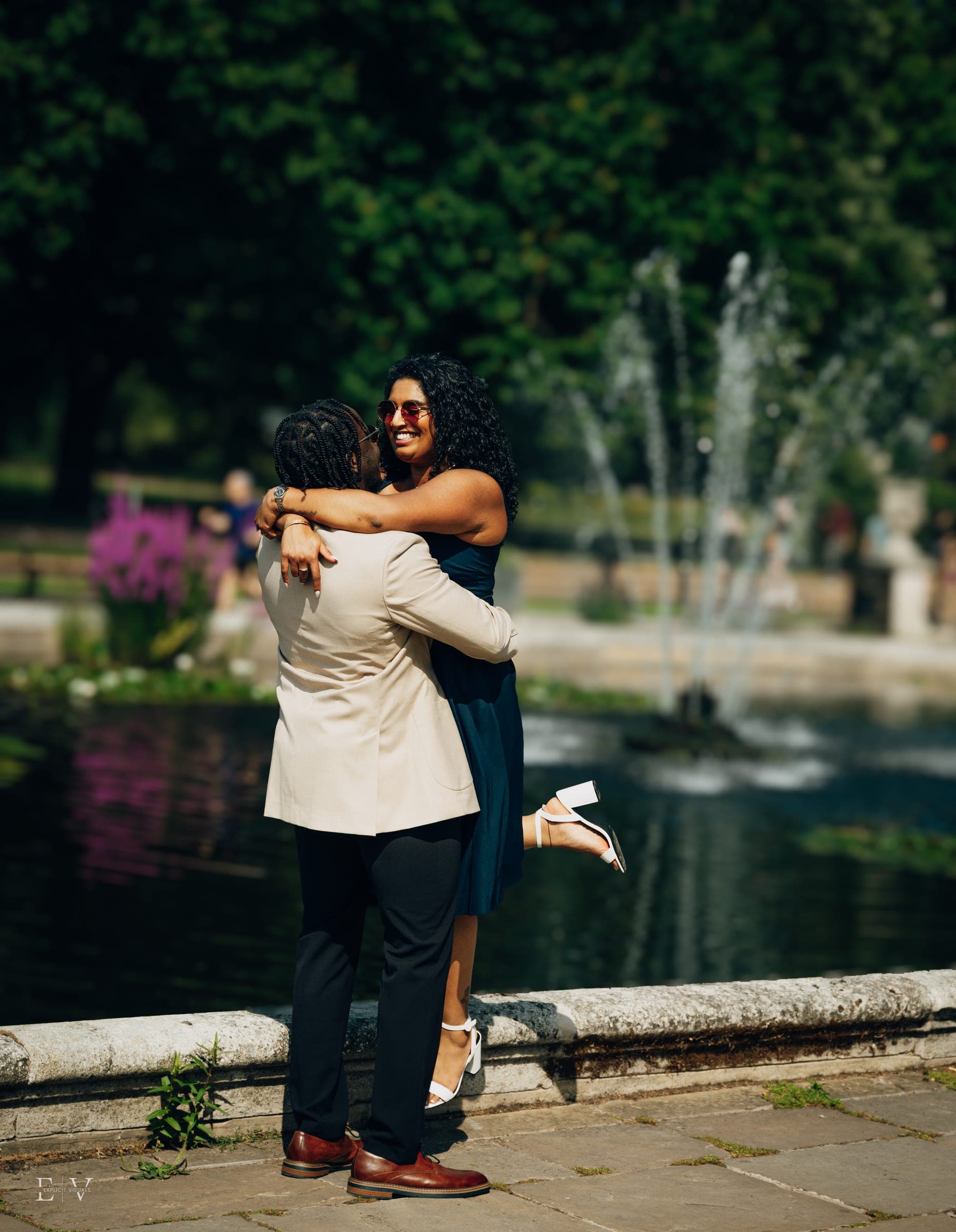 The same embrace framed closer, both laughing, water and dark green trees filling the background.