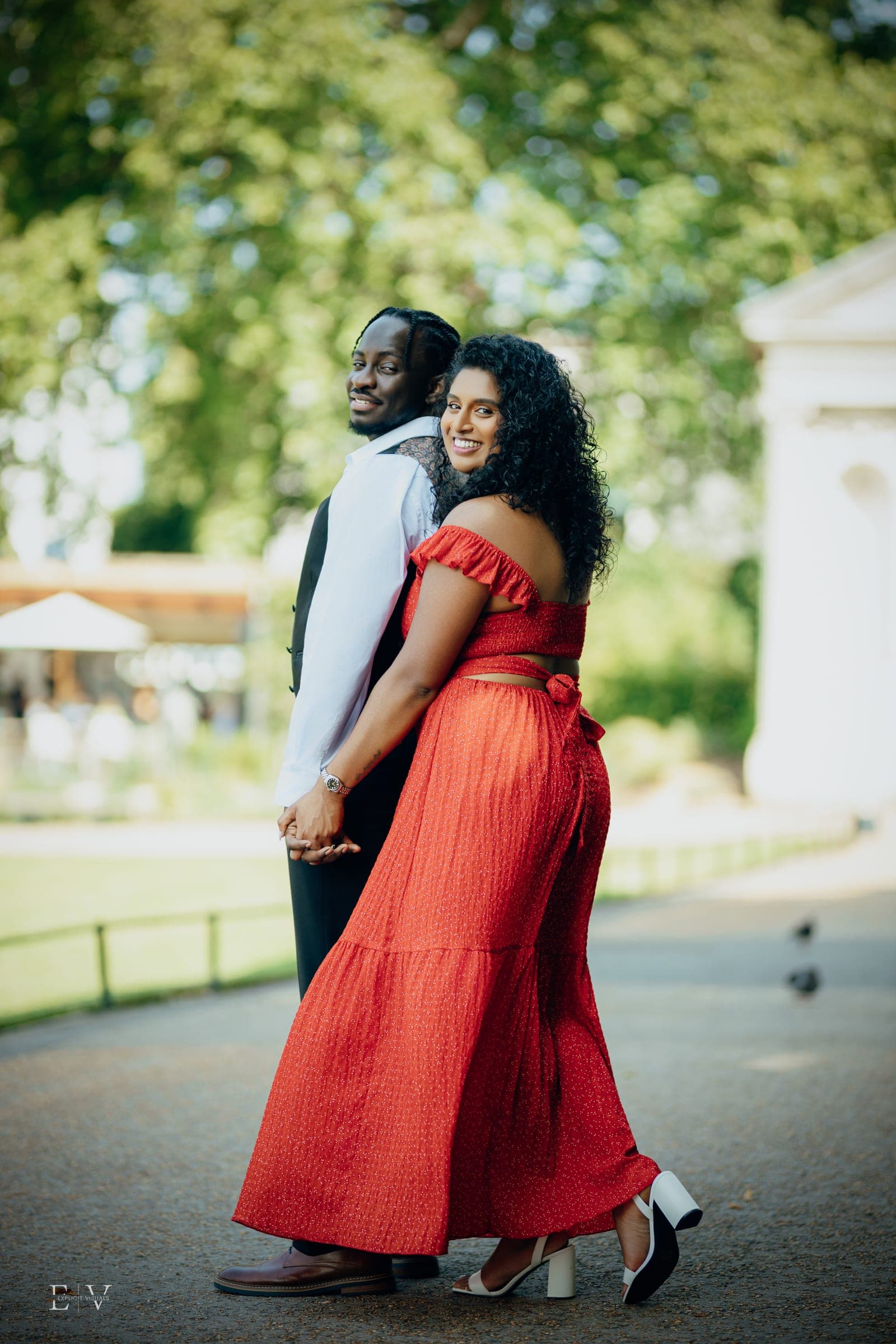 Turning back over one shoulder mid-walk, the red dress sweeping out behind, hands still joined.