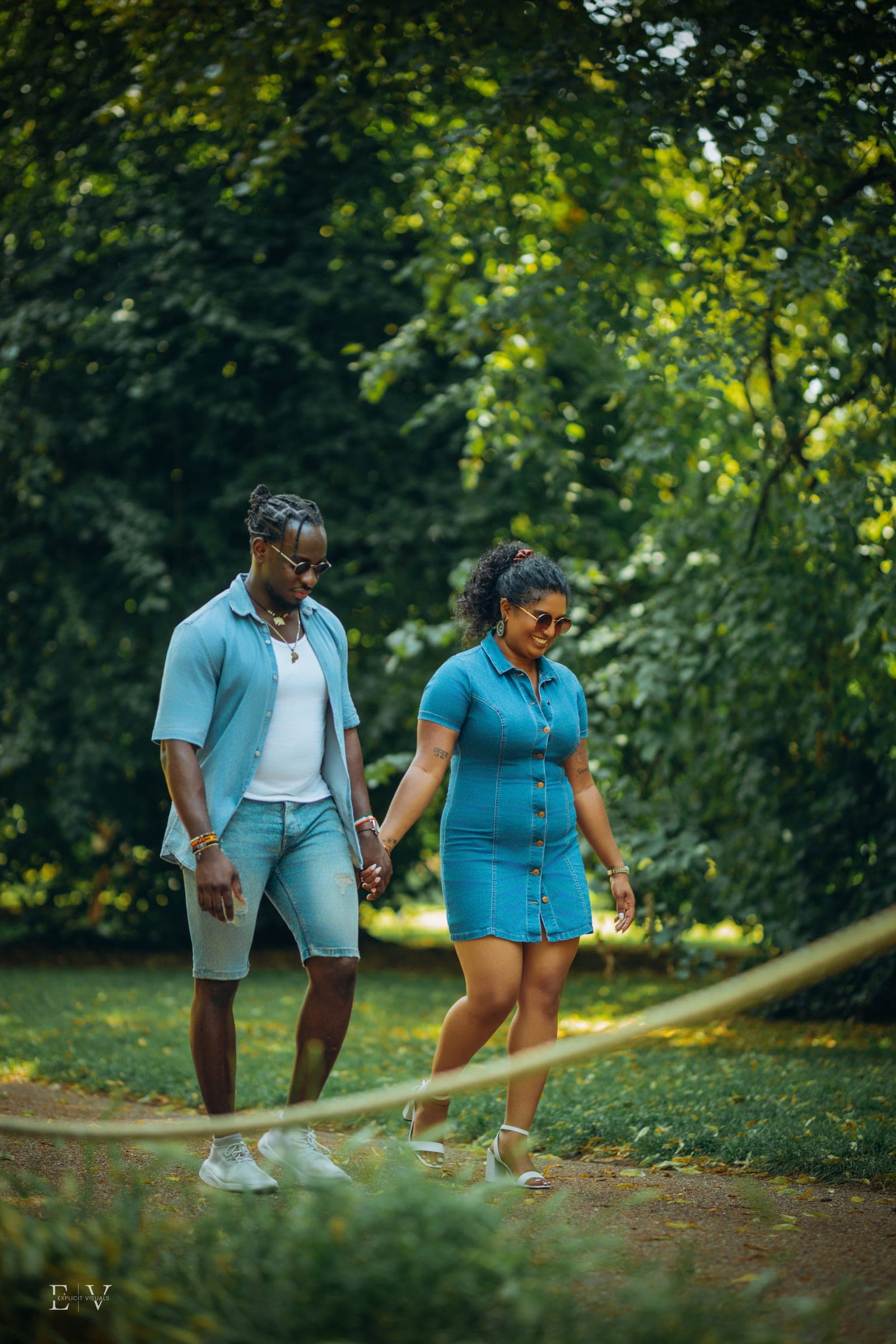 Hand in hand across the grass in matching denim, both watching their feet.