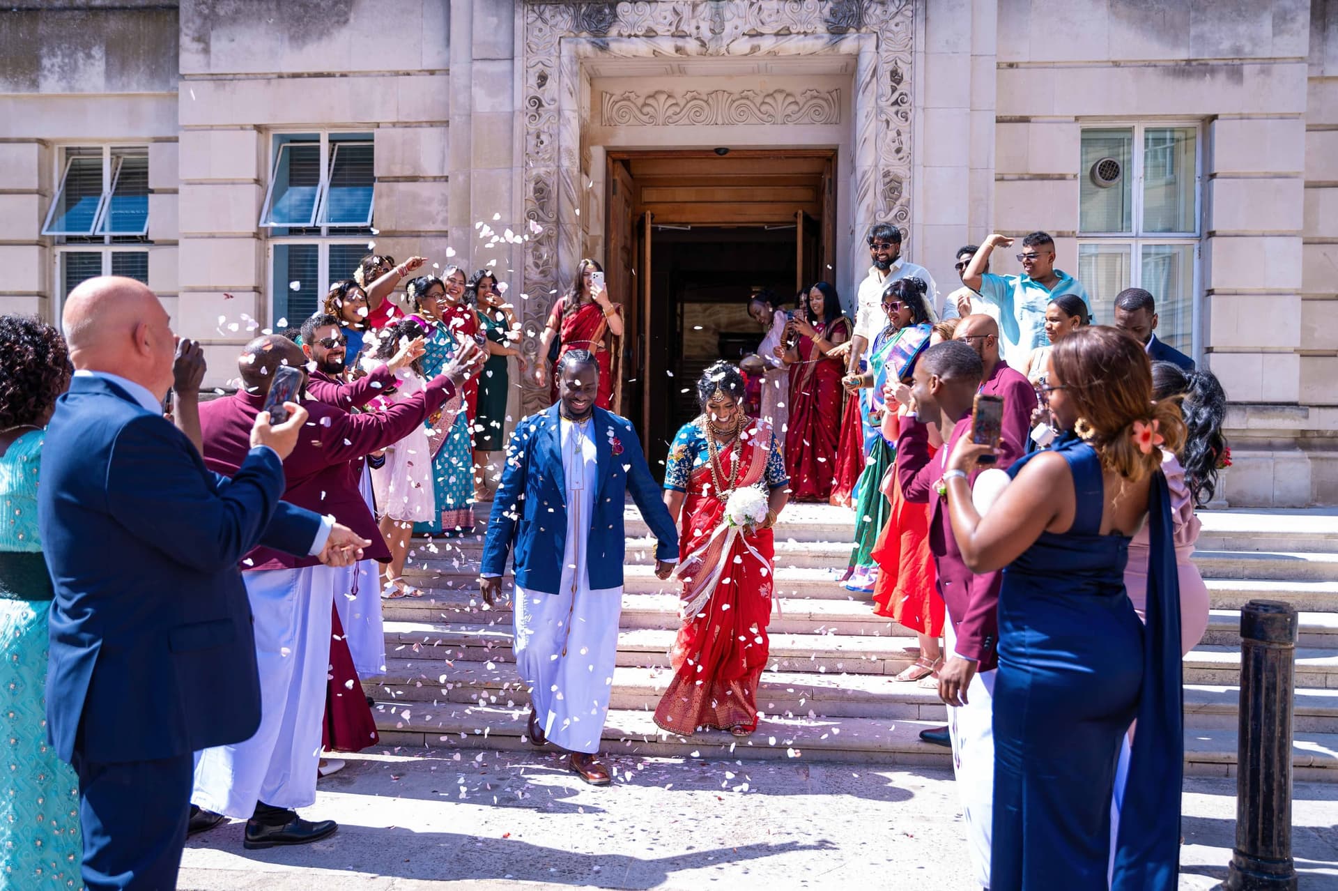The couple walk down the town hall steps hand in hand through a storm of white confetti, guests applauding on either side.