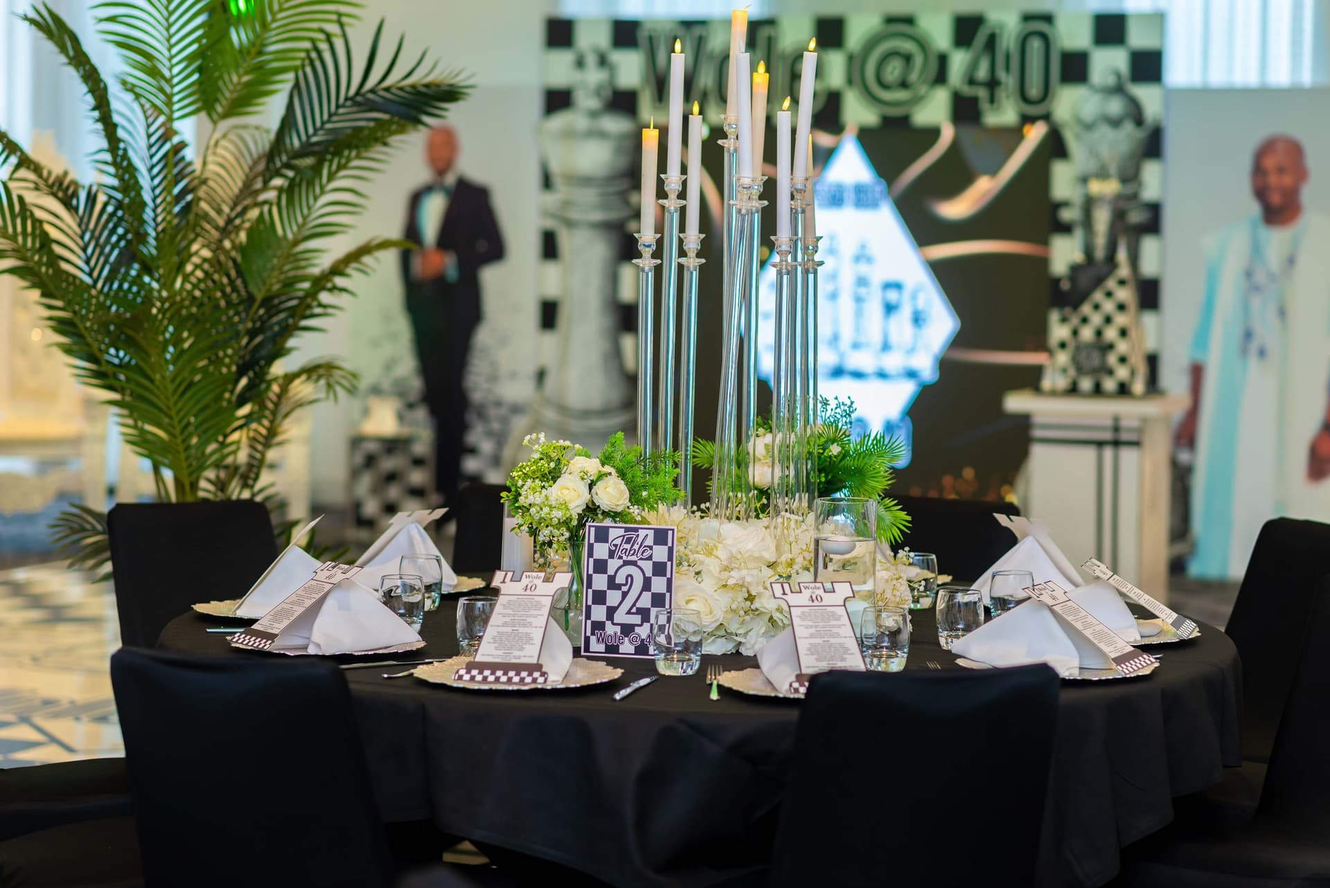 Table two, its silver candelabra lit above white hydrangeas, the chess backdrop soft in the distance.