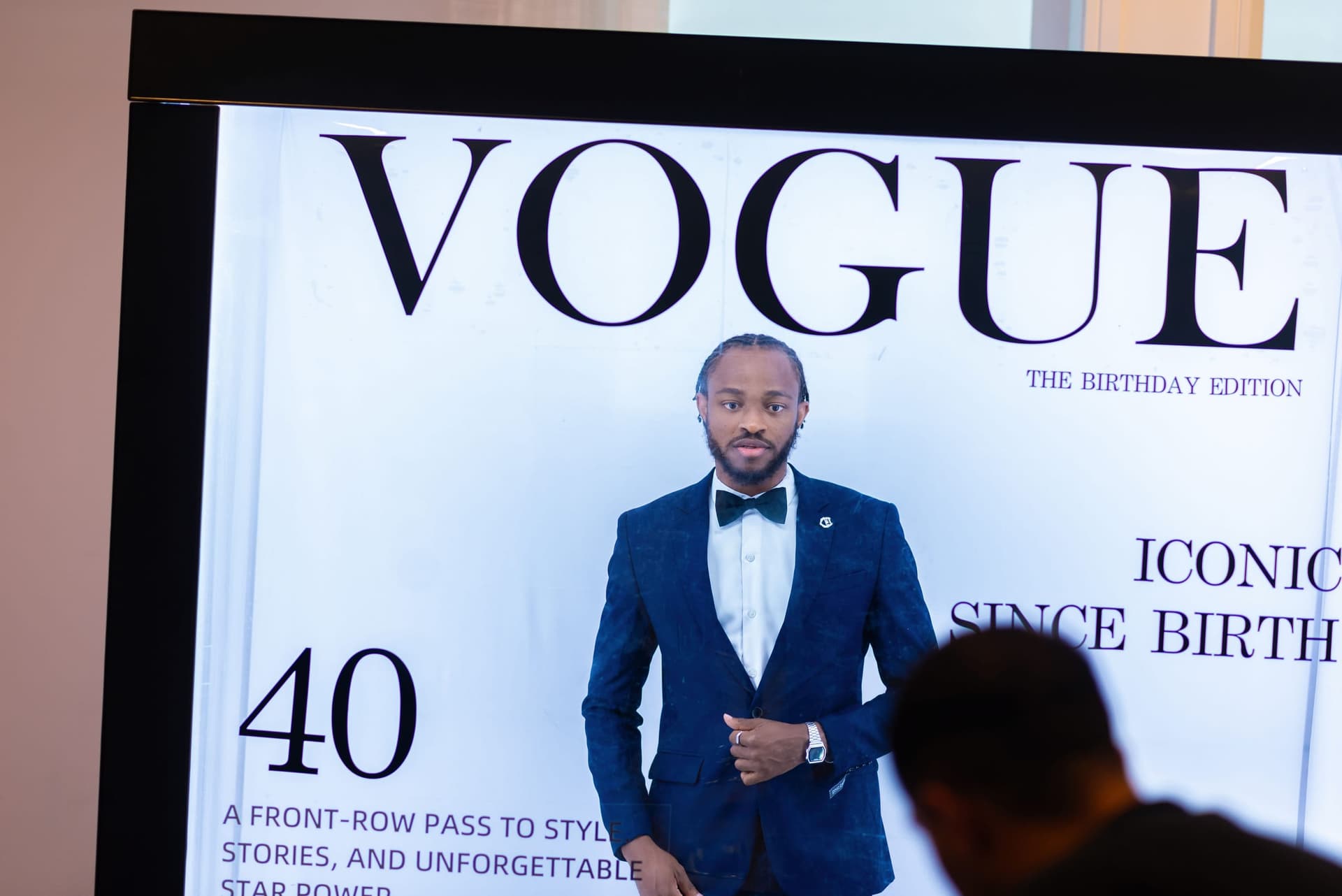 A backlit board at the entrance styled as a magazine cover, a guest walking past it in silhouette.