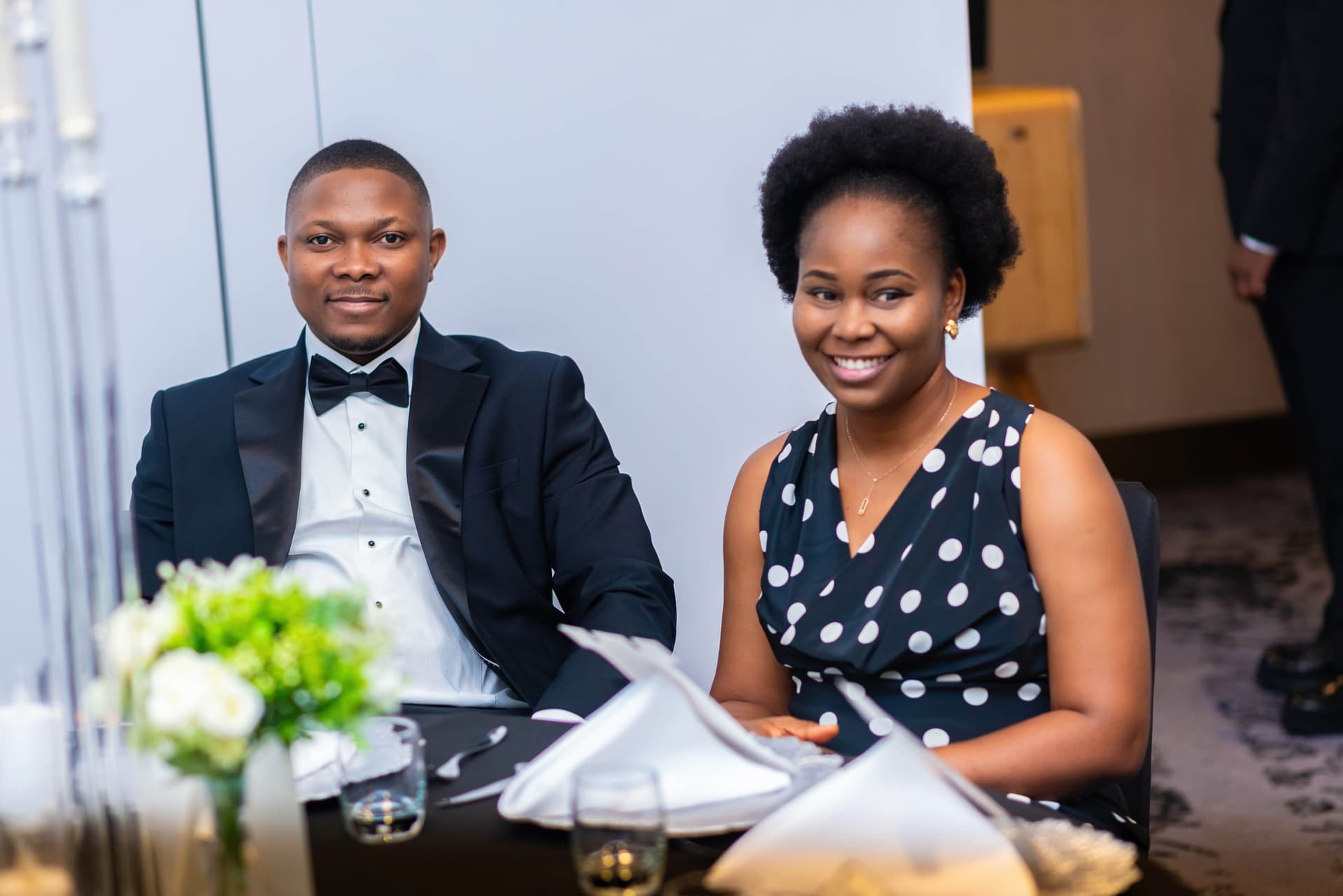 The same two a moment later, both smiling, white napkins and glasses across the table in front of them.