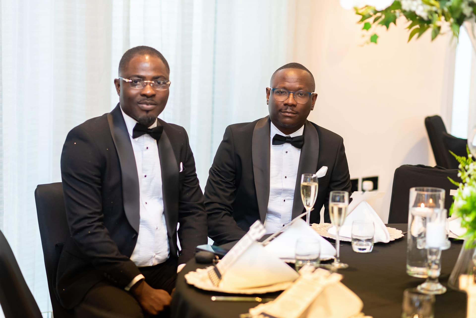 Two guests in dinner jackets seated side by side, champagne poured, candles burning down the table.
