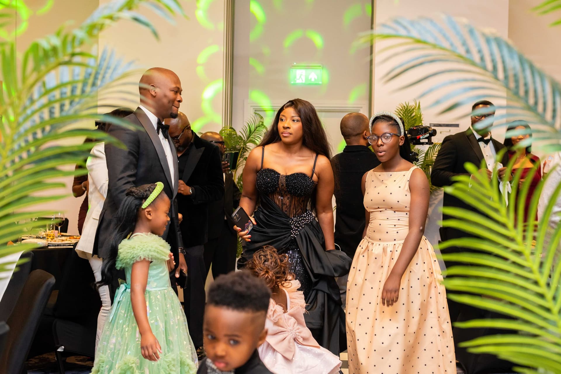The family crossing the floor together between the palms, guests and crew in the background.