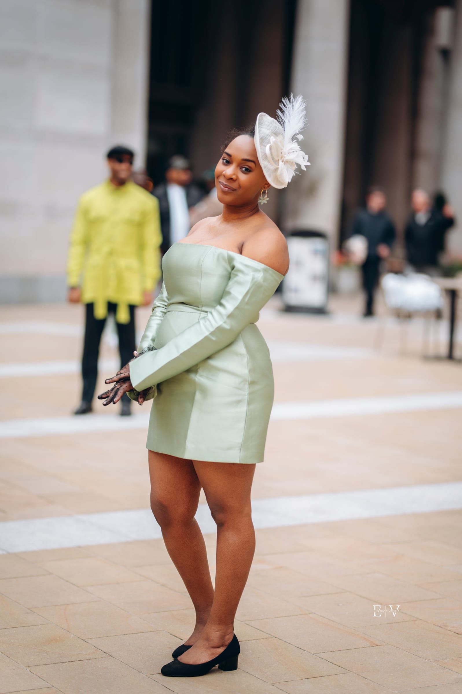 The same dress from behind and to the side as she turns back to the camera, smiling, black court shoes on the pale paving.