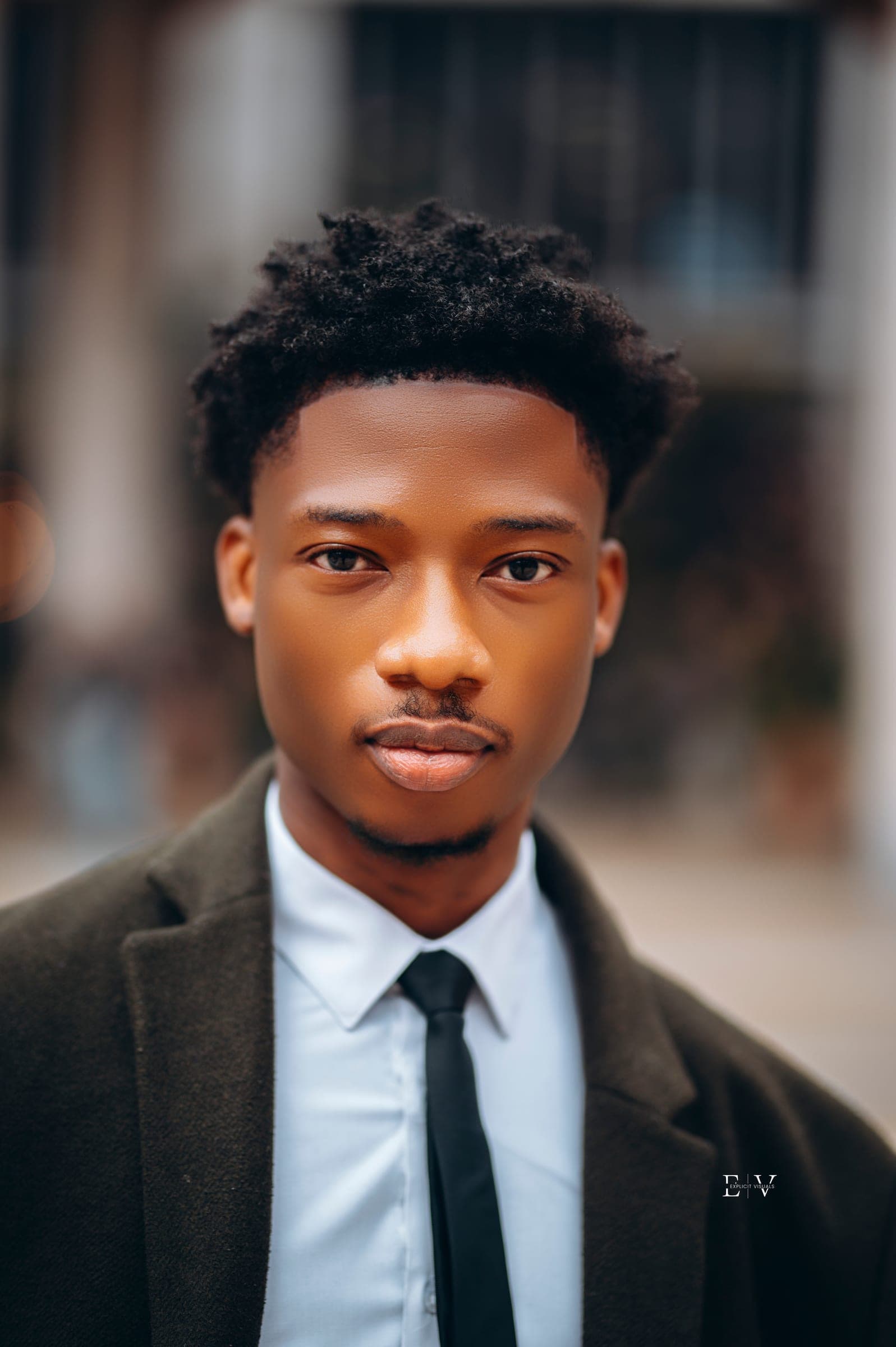 A close portrait of the same young man, the overcoat collar turned up, the square soft and pale behind him.