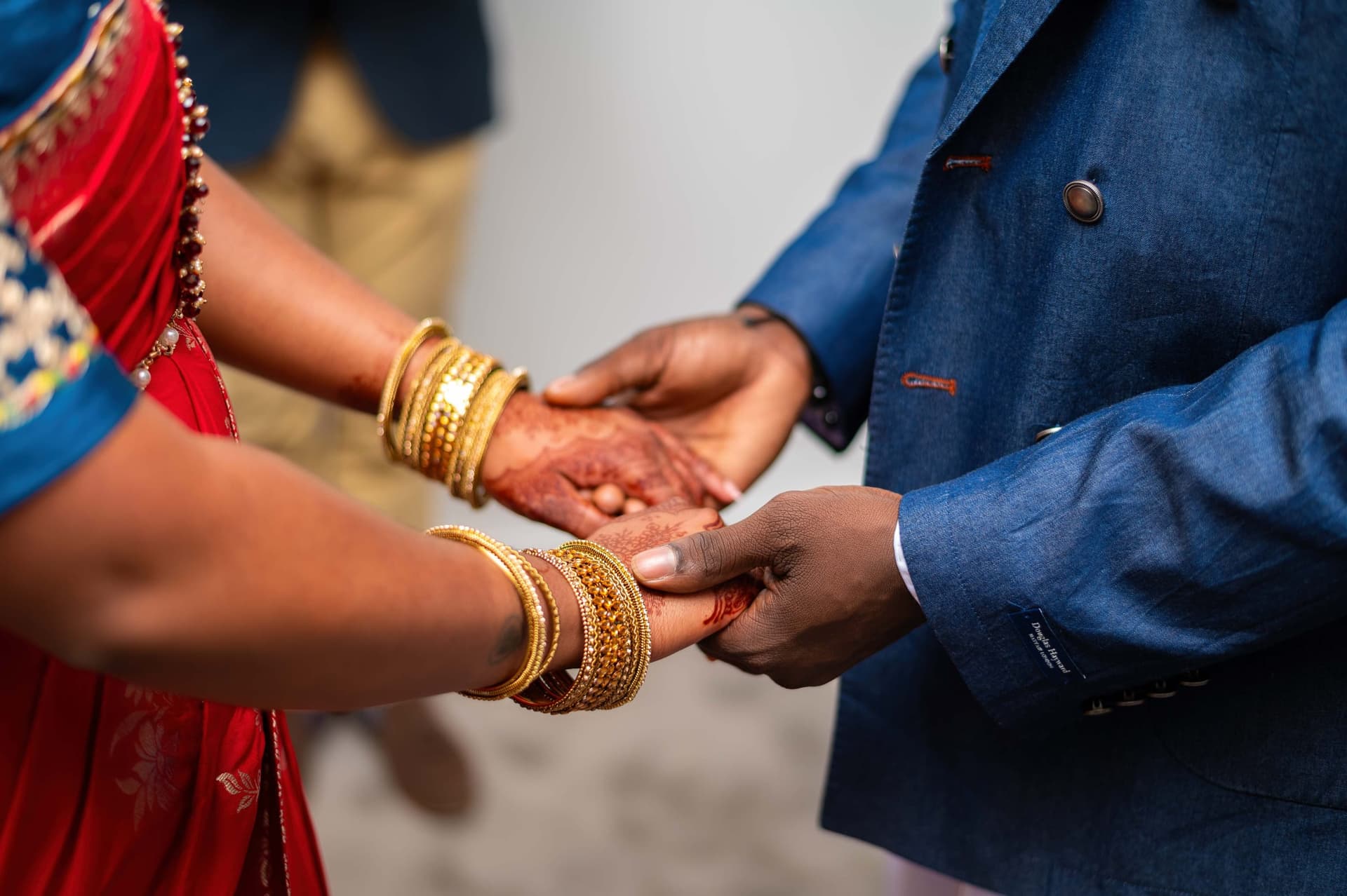 Close in on their joined hands — her henna and stacked gold bangles against his cuff.
