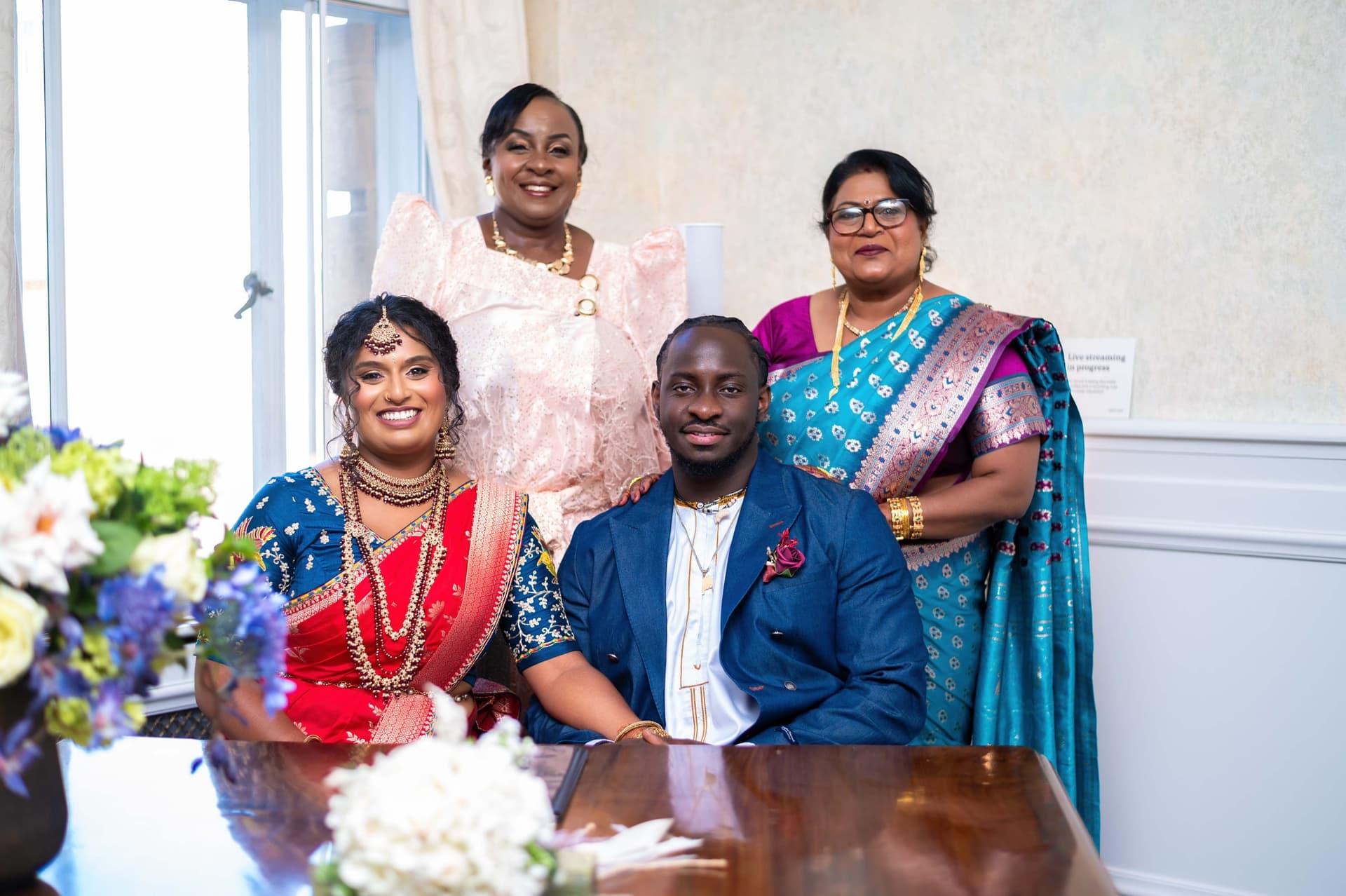 The couple seated at the signing table with both mothers standing behind them.