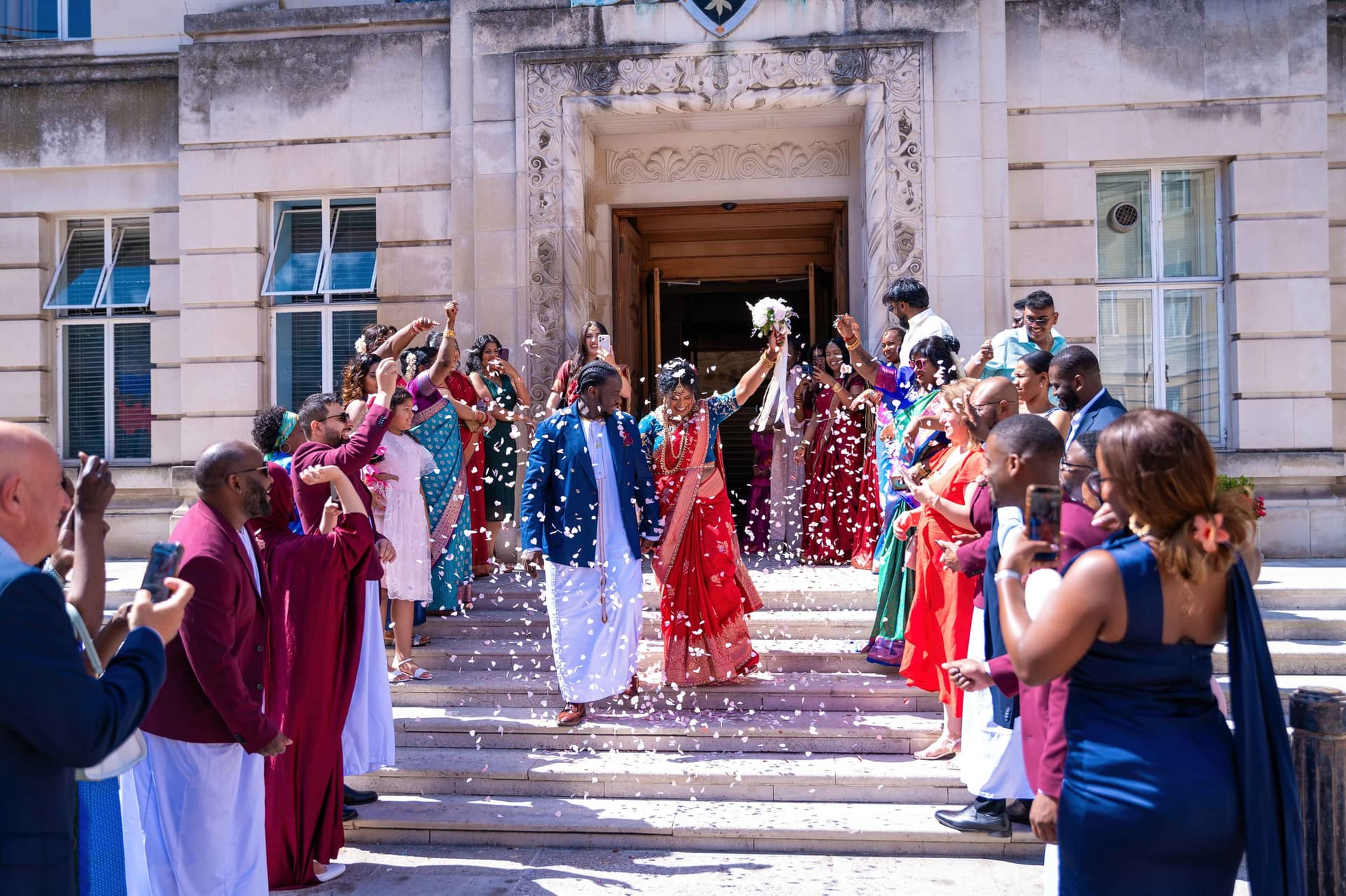 Guests line both sides of the town hall steps throwing white confetti as the couple come down through it.