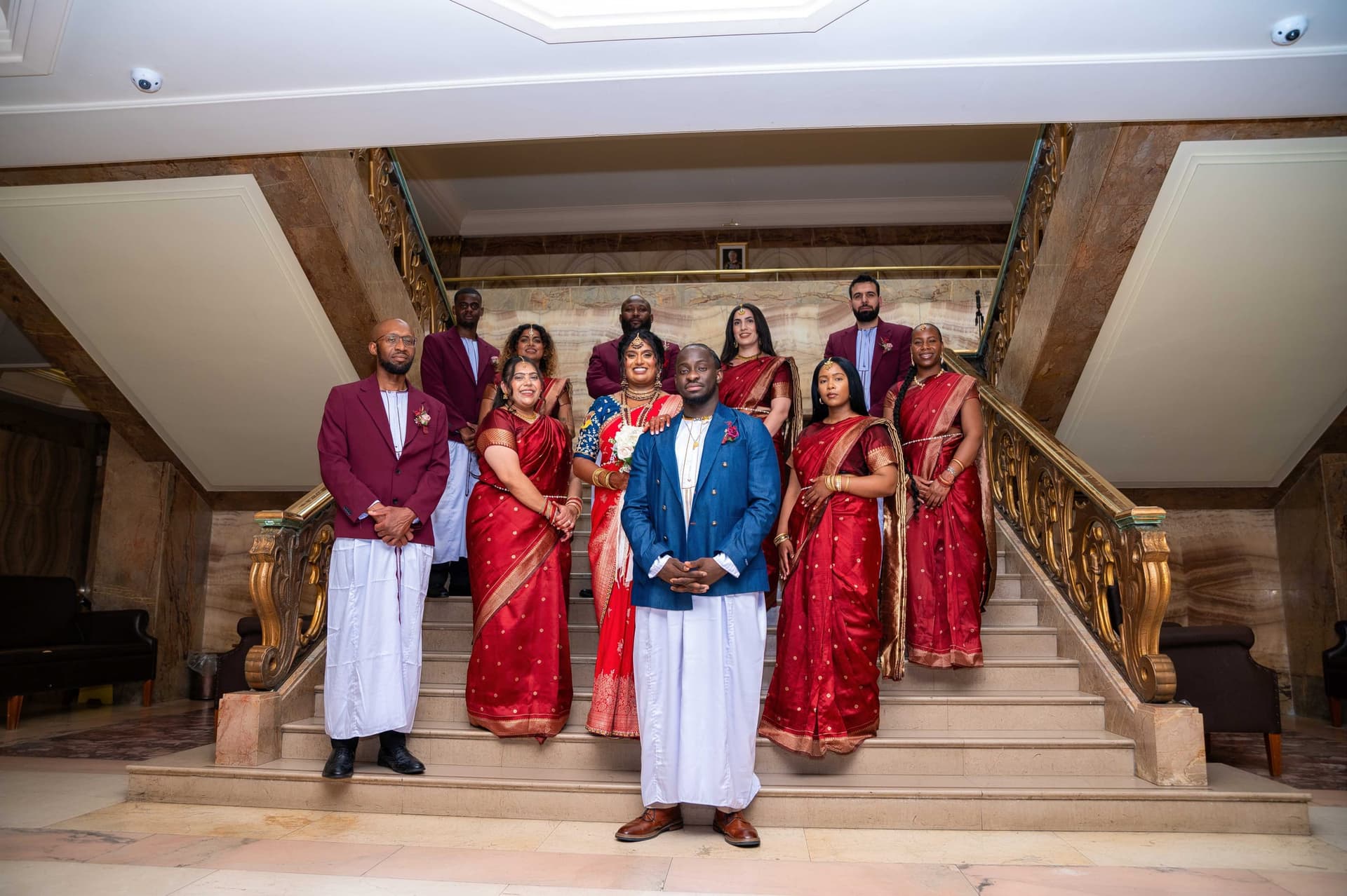 The party spread across the width of the gilded staircase, the groom standing alone on the bottom step.