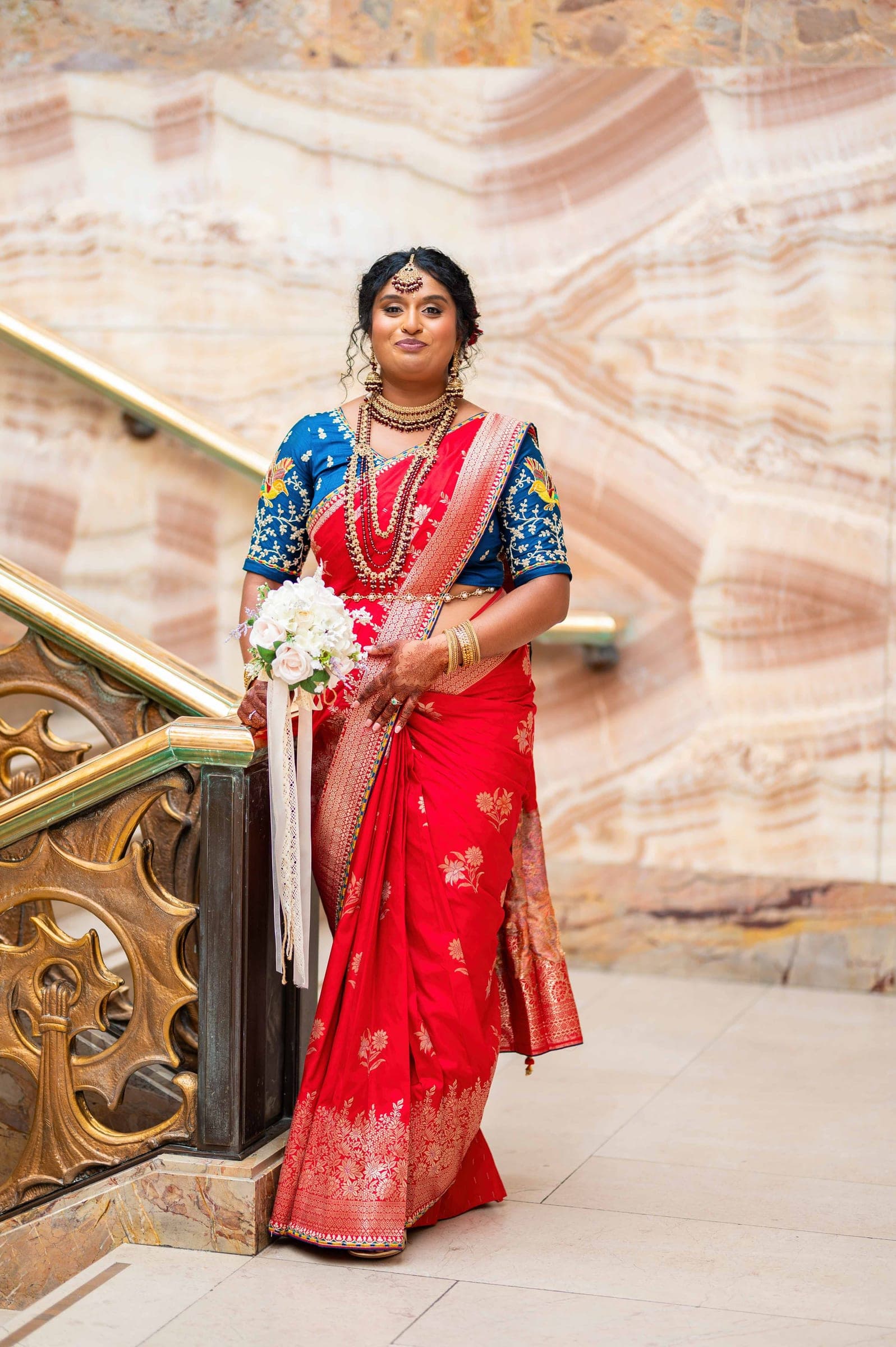 A full-length portrait of the bride against a marble wall, one hand resting on the gilded banister.