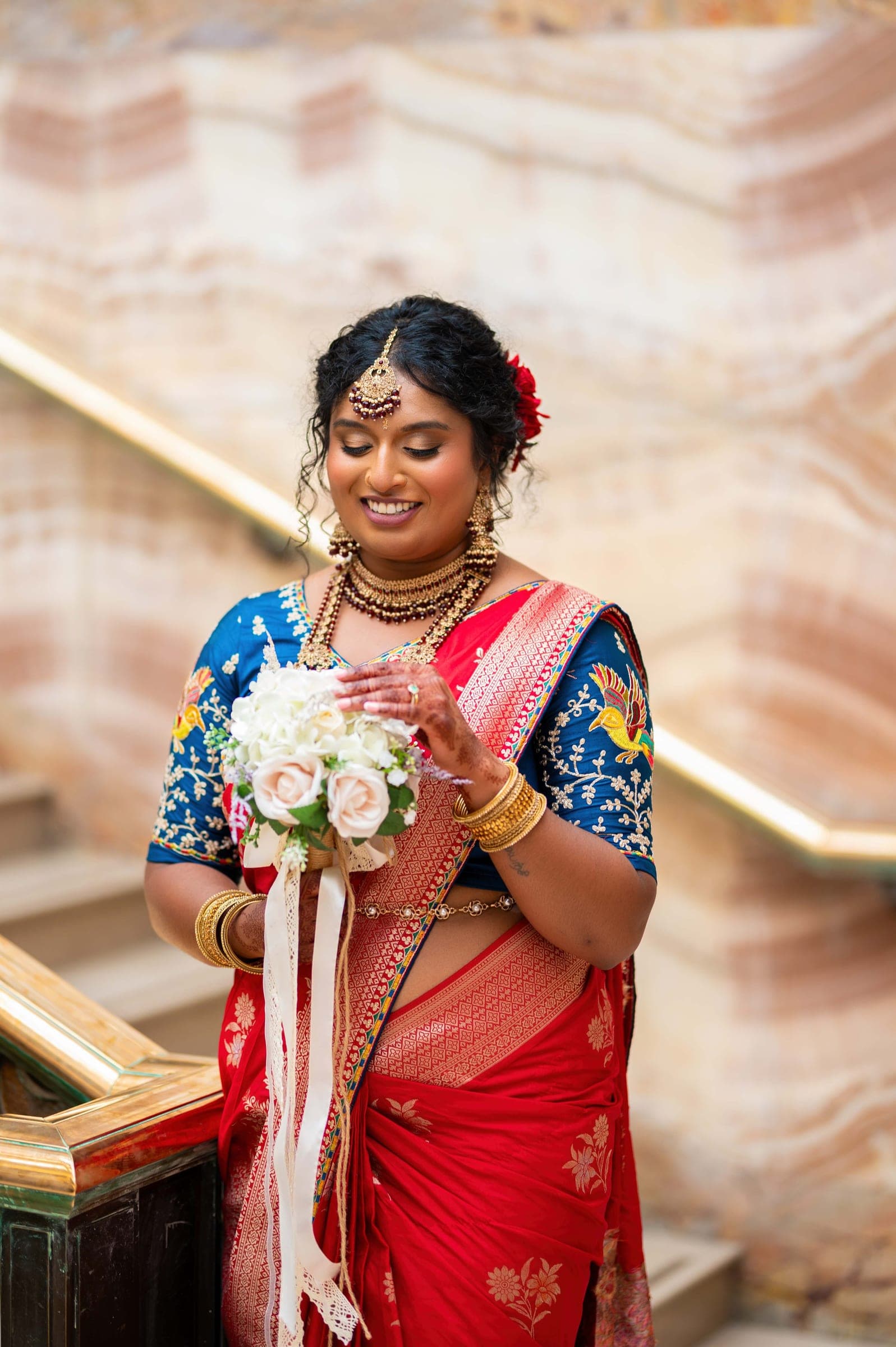 The bride looks down at her bouquet and smiles, bangles stacked along both wrists.