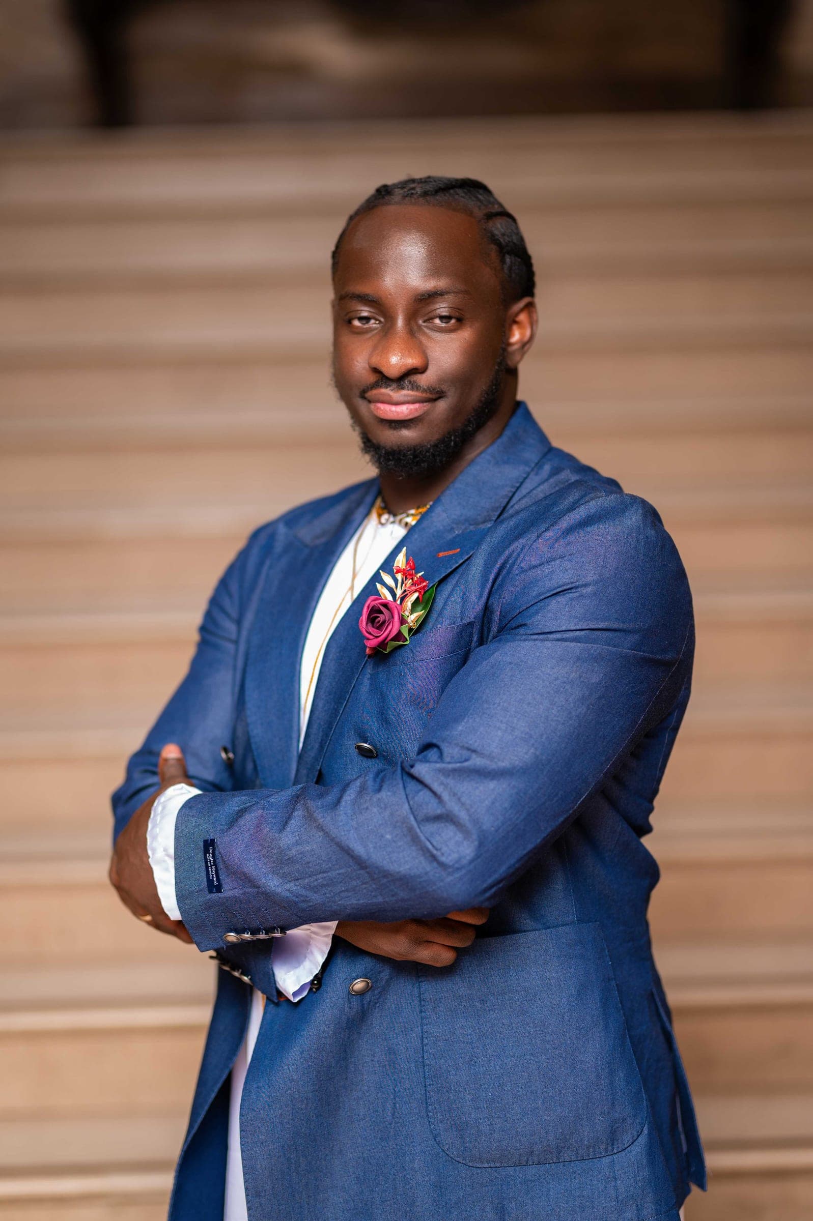 The groom with his arms folded, standing against the pale stone steps.