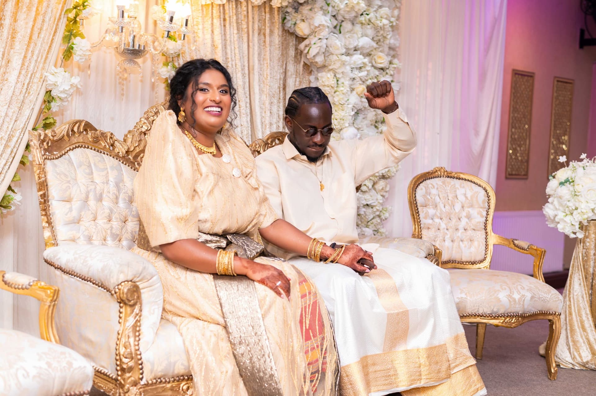 The two of them seated on gold thrones at the reception, one arm thrown up in celebration.