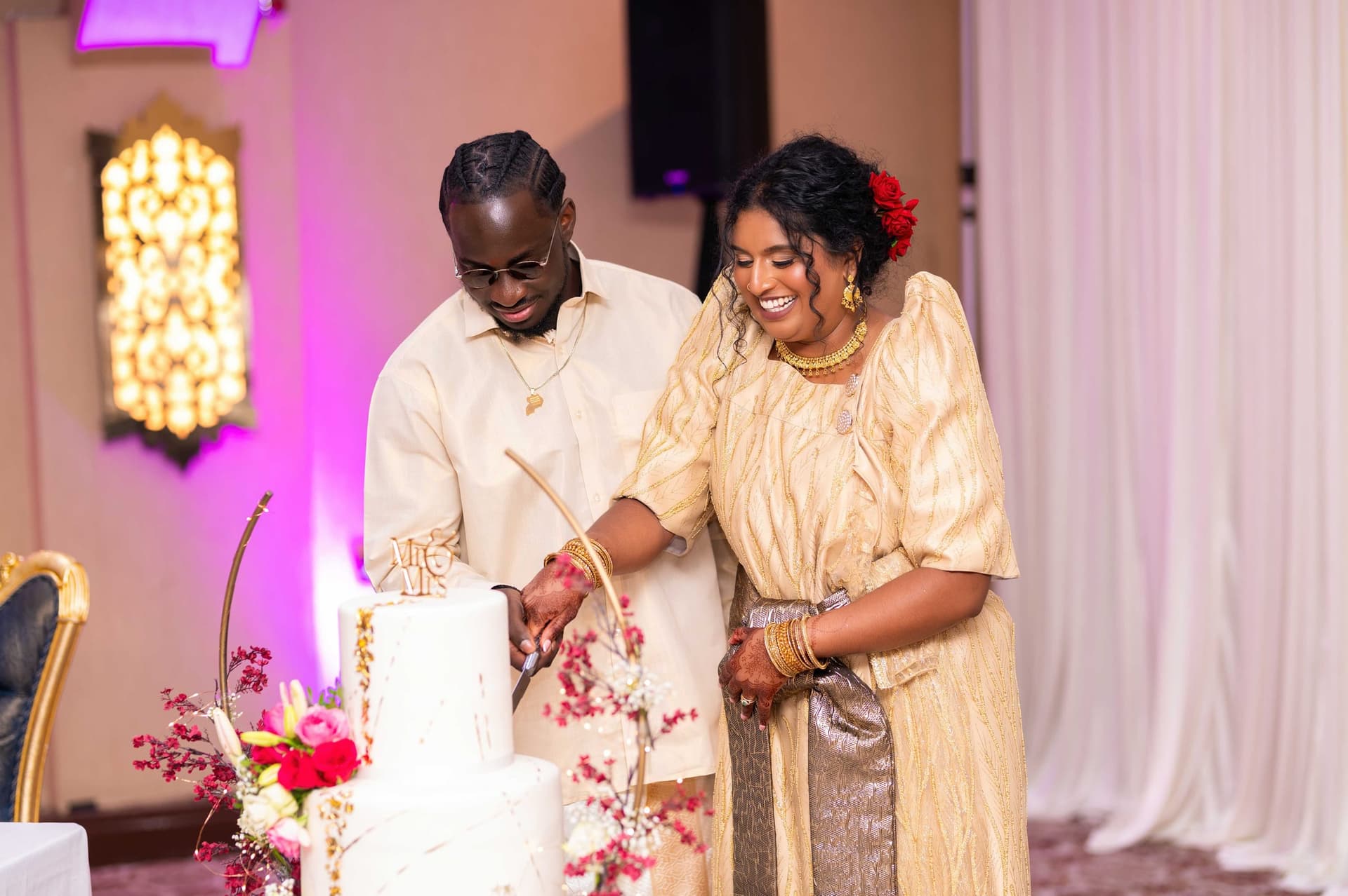 Cutting the tiered white cake together under the reception lights.