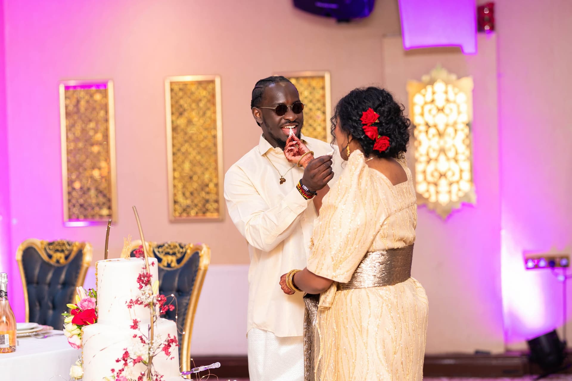 Feeding each other the first bite of cake, the room lit purple behind them.