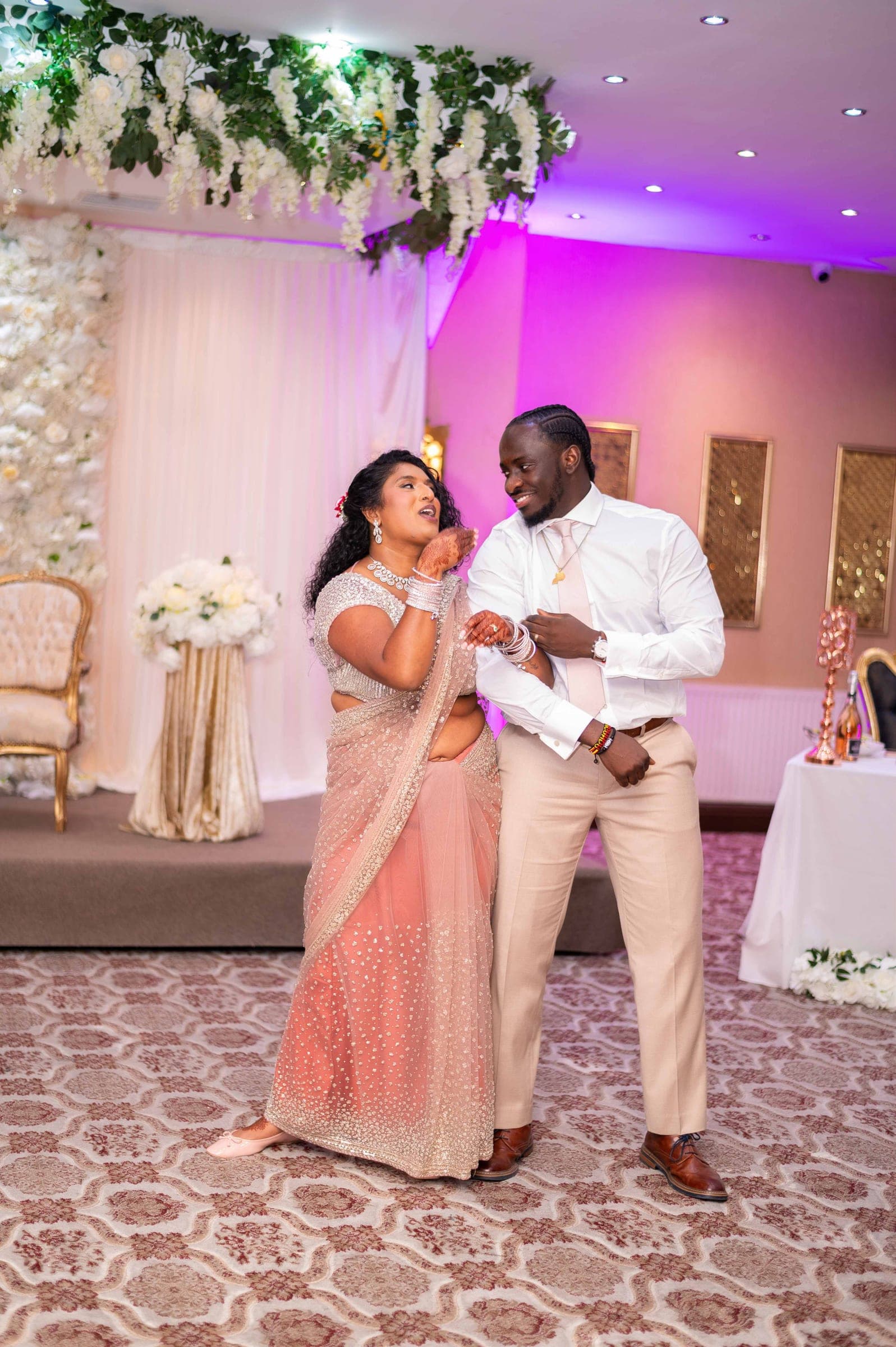 The two of them dancing together on the reception floor under the flower canopy.