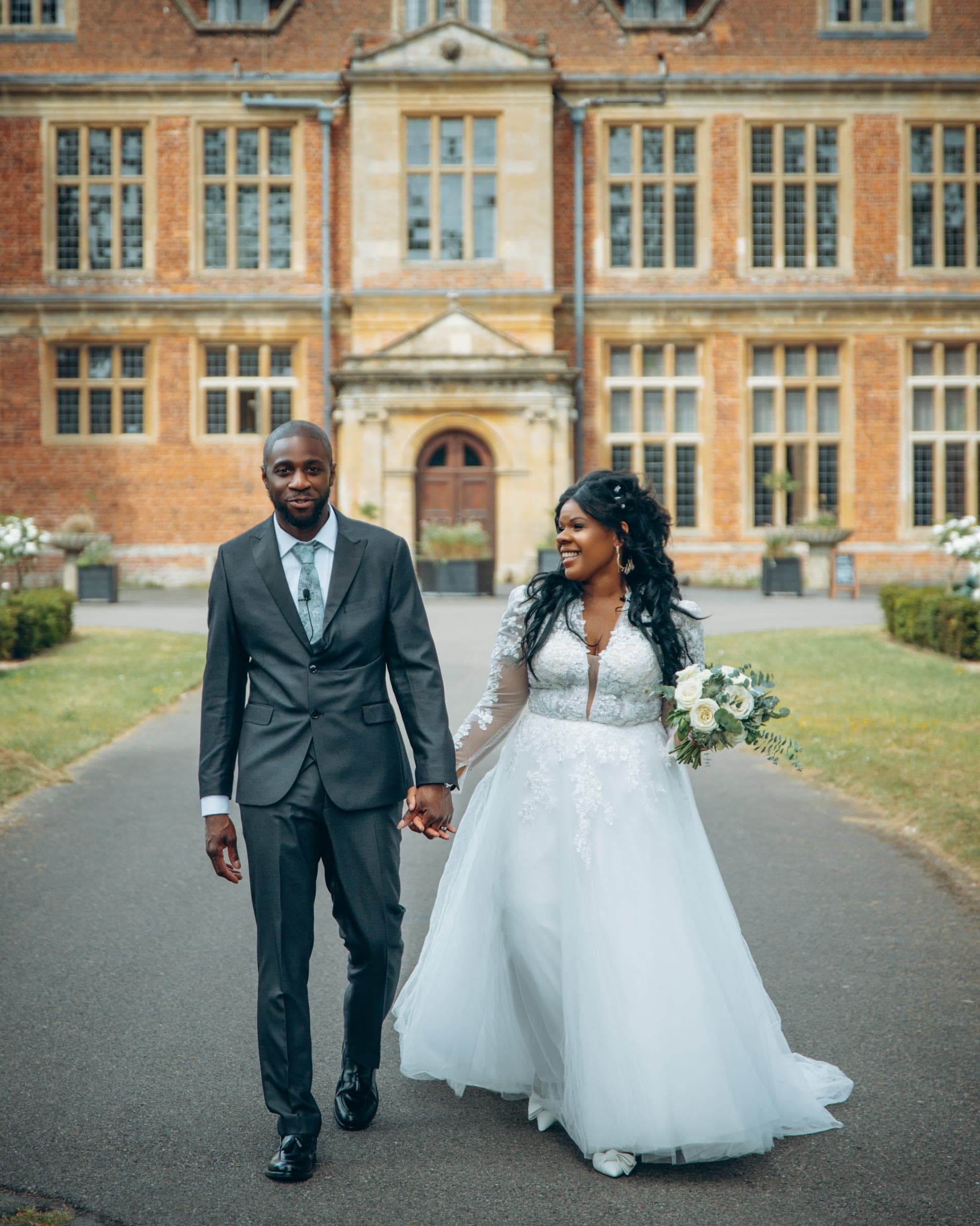 Framed tighter on the couple mid-stride, the manor's arched doorway centred behind them.