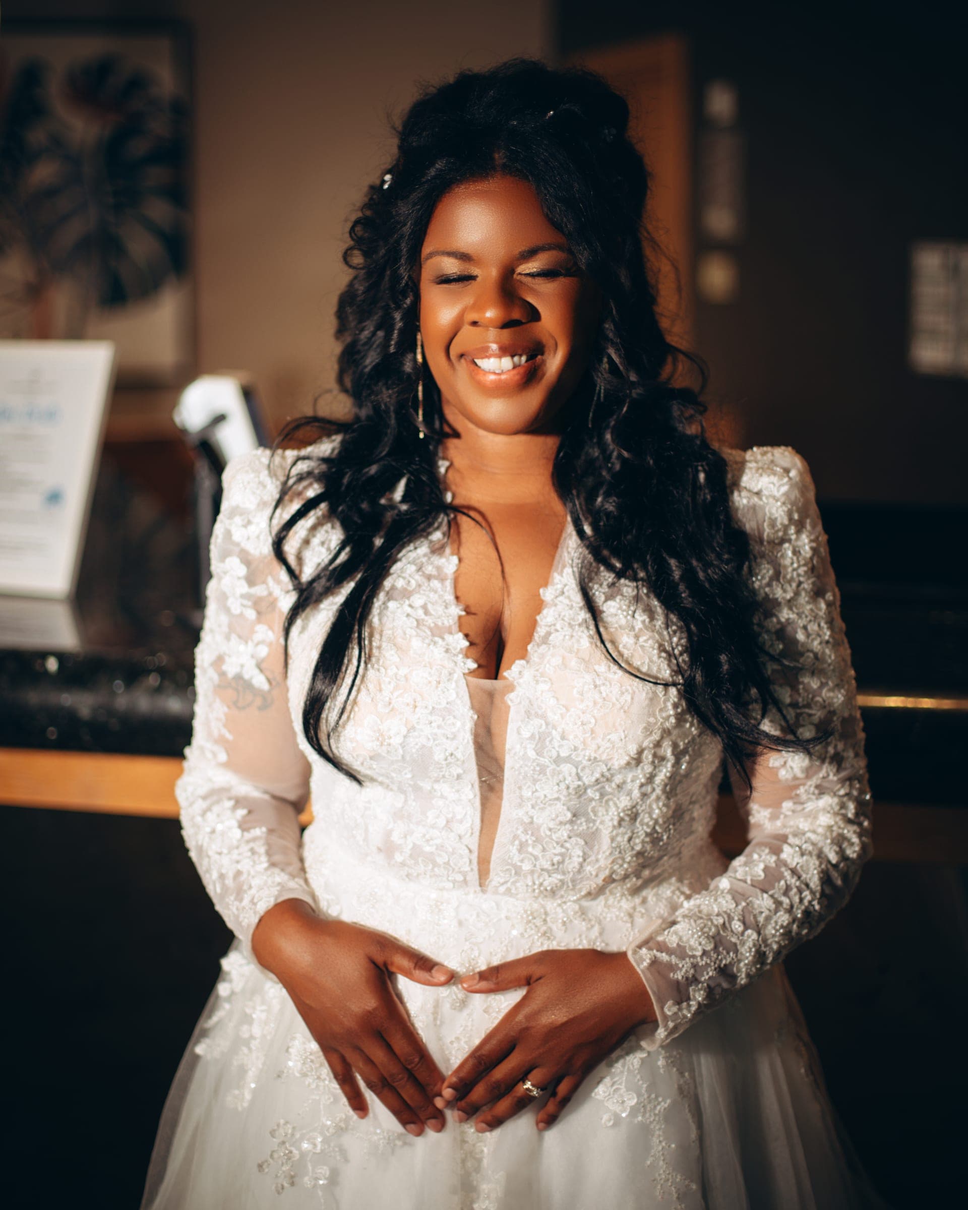 A close portrait of the bride laughing with her eyes closed, hands folded at her waist.