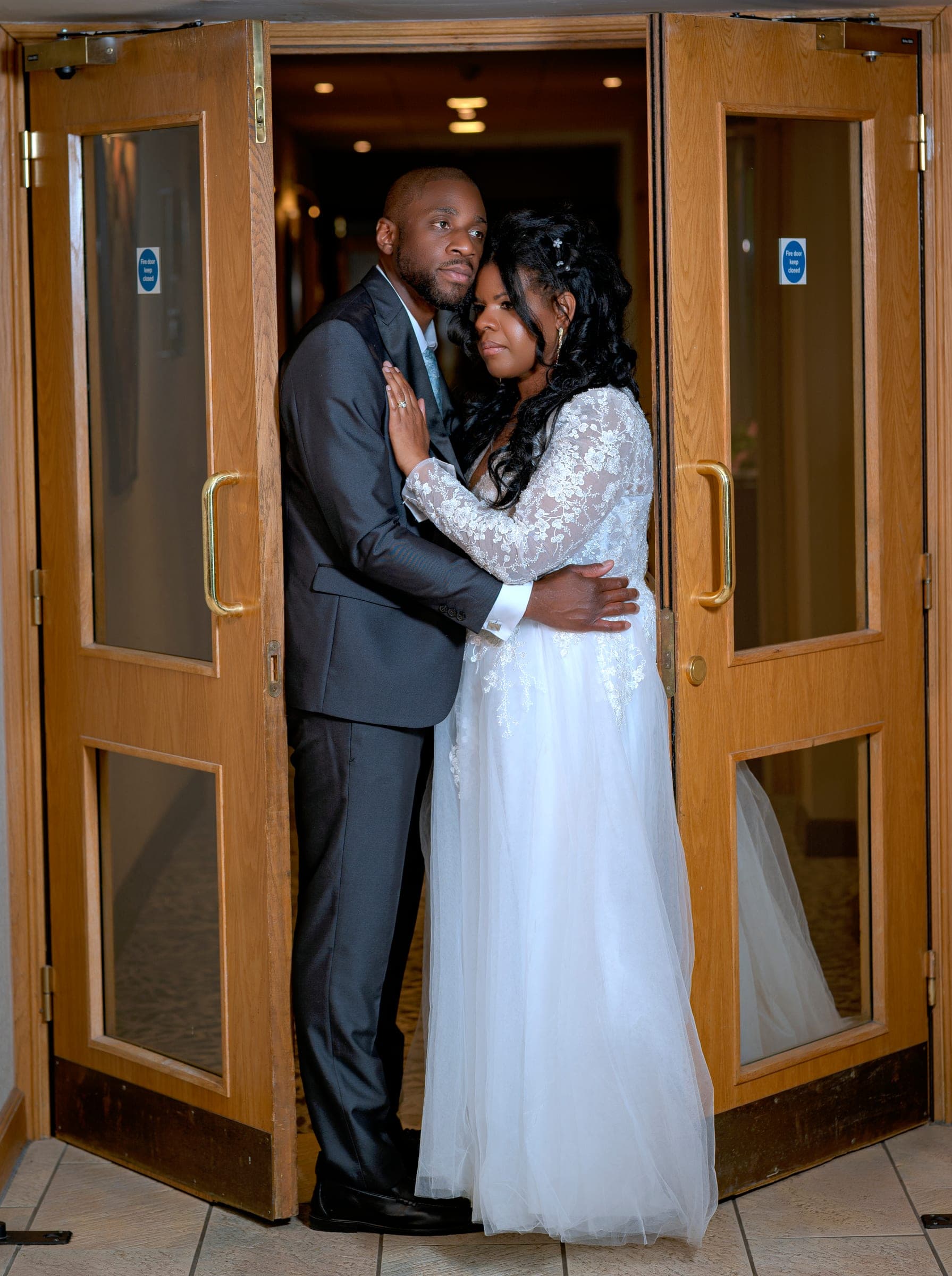 The couple hold each other in an open doorway, framed by the timber doors on both sides.